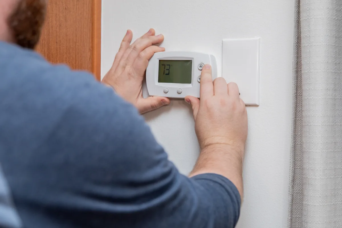Rear view of a technician checking a wall thermostat