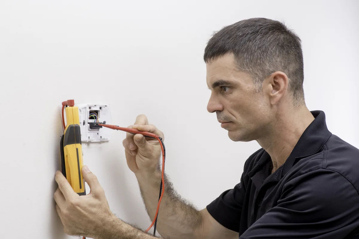 Technician testing electrical connections at an uncovered thermostat