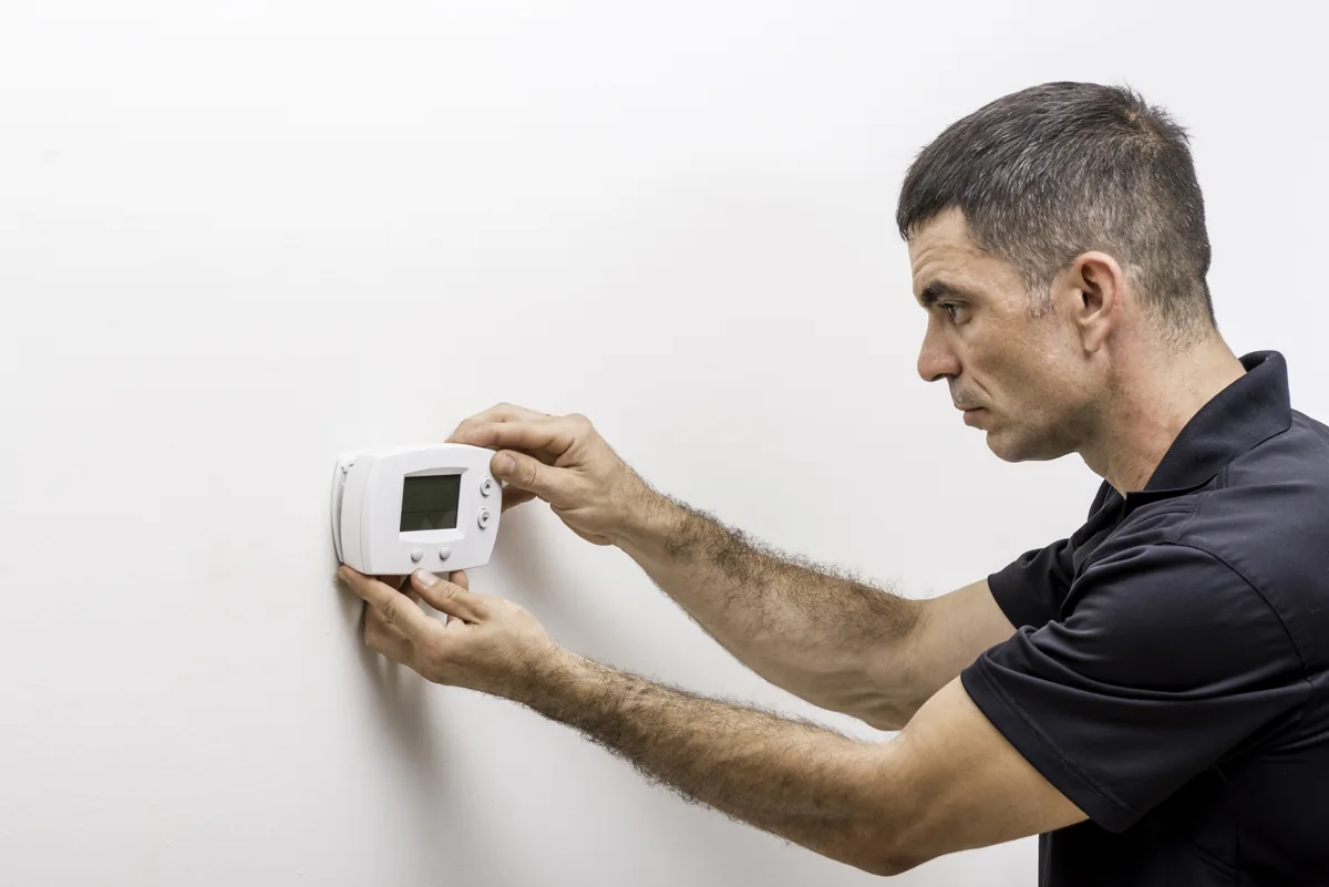 Technician adjusting temperature controls on a wall thermostat