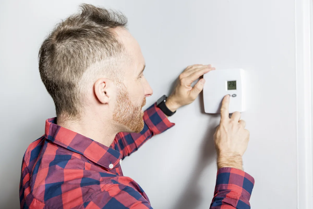 Technician in a plaid shirt adjusting a wall thermostat