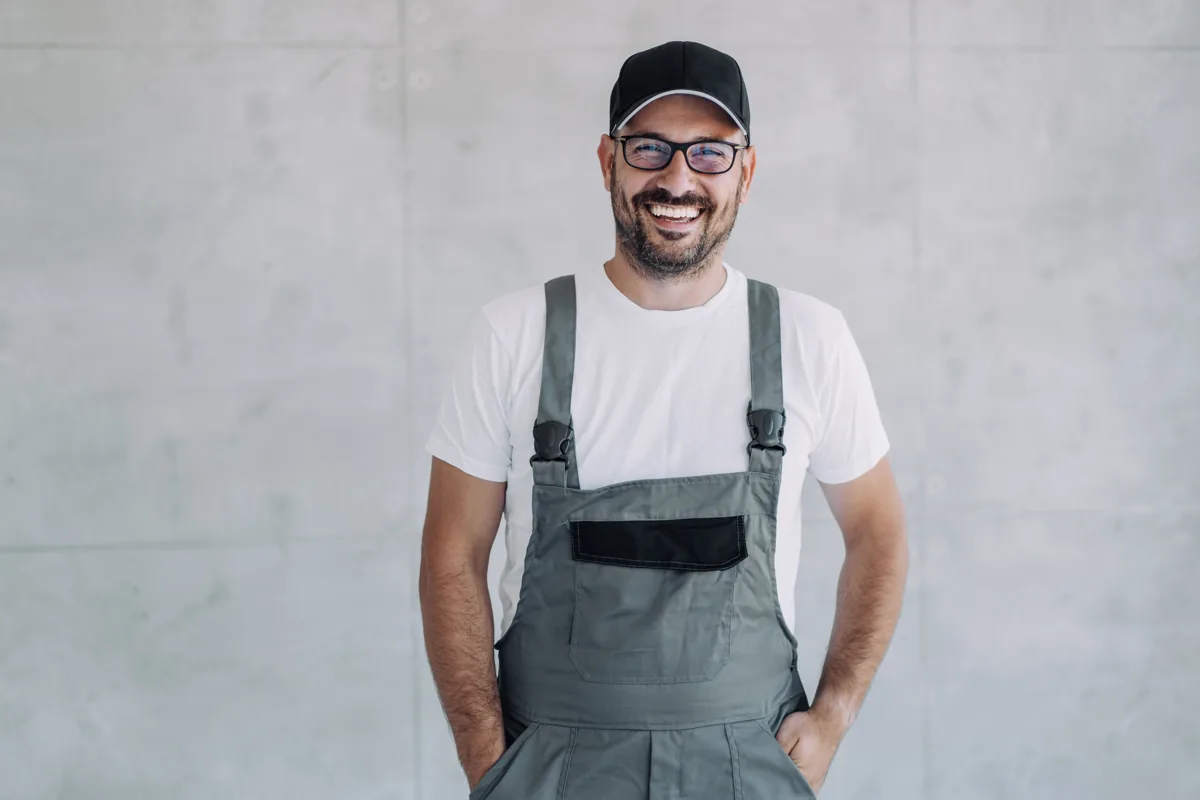 Technician wearing a cap, glasses and grey overalls indoors