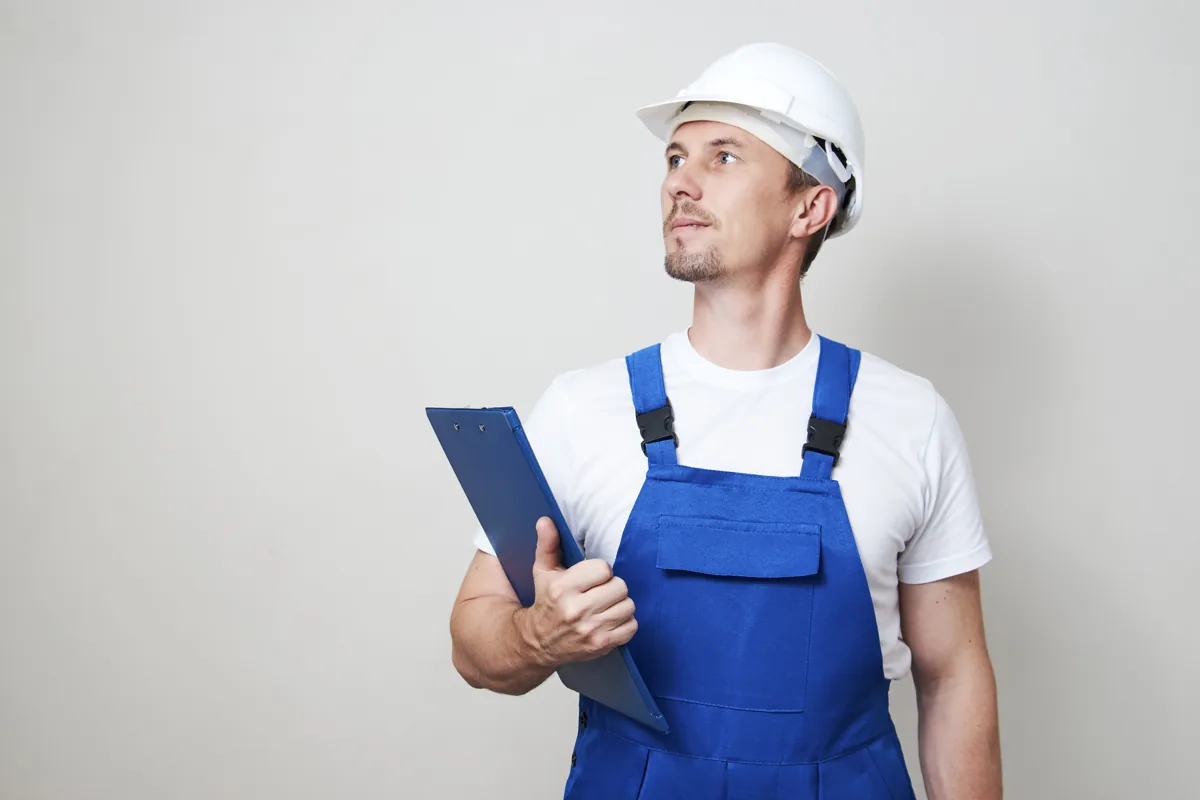 Technician wearing a hard hat and holding a clipboard indoors