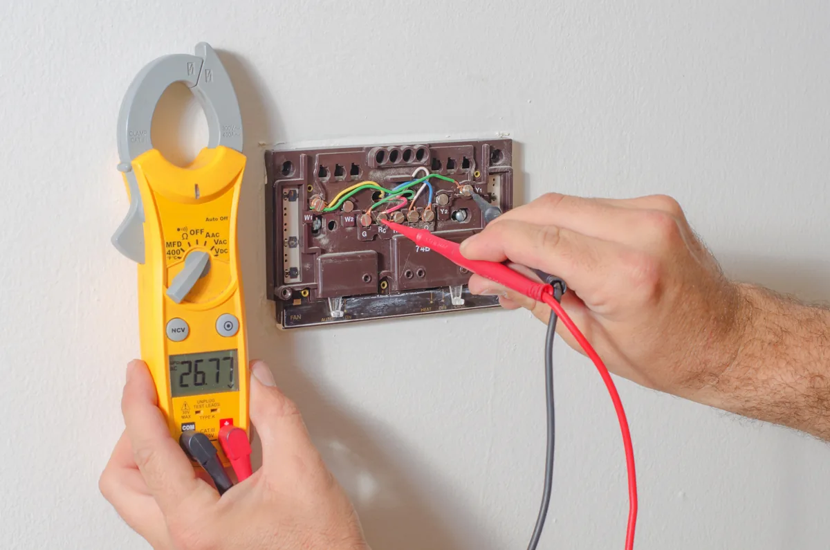 Technician testing thermostat wiring with a digital multimeter