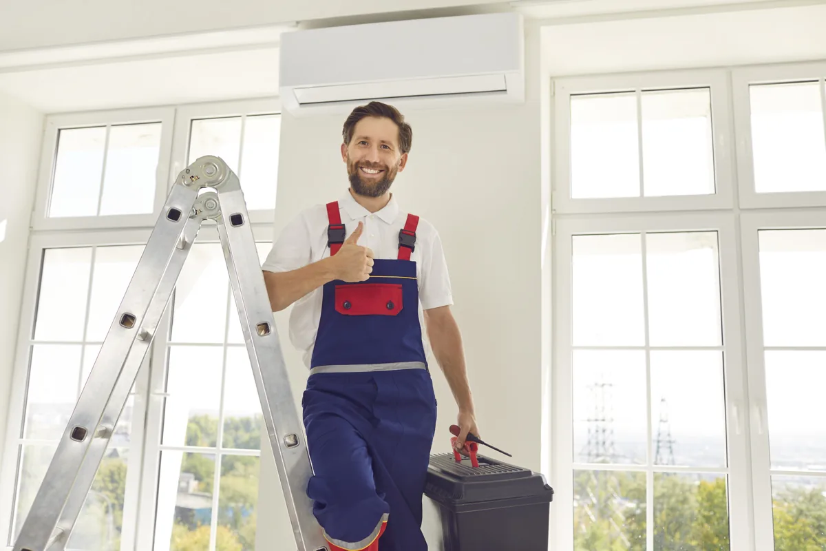 Technician carrying a toolbox beside a ladder indoors
