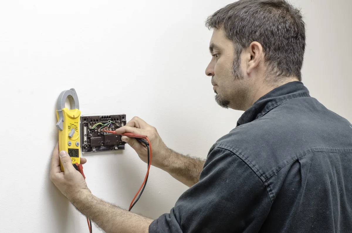 Technician using meter probes to check wall thermostat wiring
