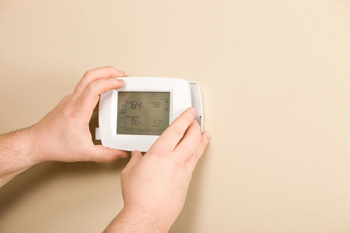 Hands adjusting a wall-mounted thermostat